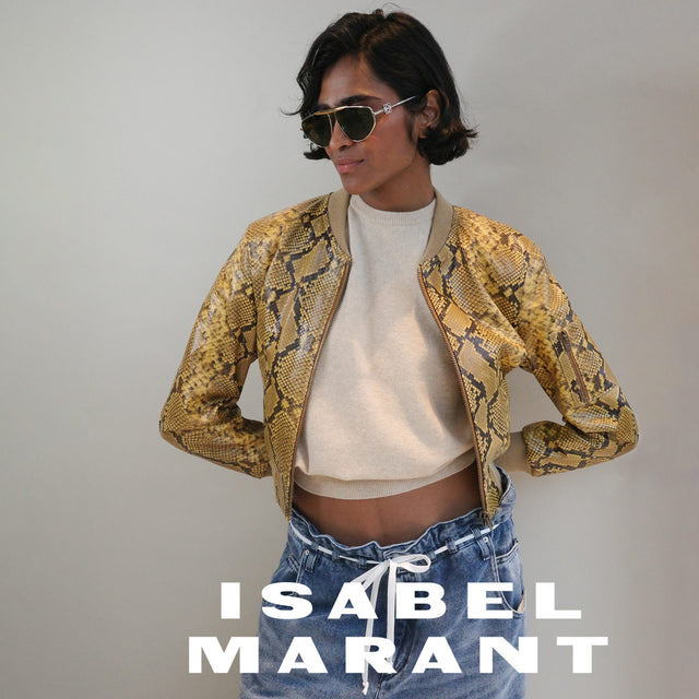 Woman wearing yellow and black snake pattern leather cropped jacket and blue denim jeans with white string belt, both by designer Isabel Marant 