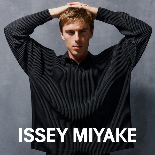 Man wearing a black ribbed sweater with 'Issey Miyake' branding on a gray background 