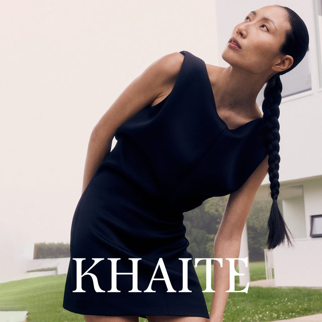 Woman wearing a black dress with 'KHAITE' branding in an outdoor setting. 