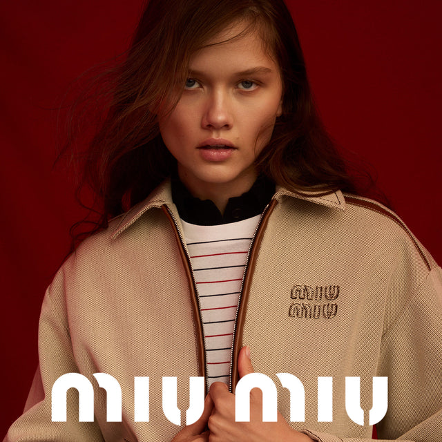 Woman wearing light brown bomber jacket with Miu Miu logo at the chest 