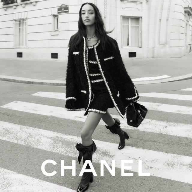 Model wearing a Chanel outfit on a city street with the brand name displayed. 