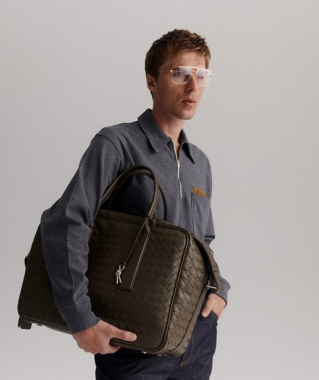 Man holding a brown Bottega Veneta leather weekender wearing a grey wool collared shirt 