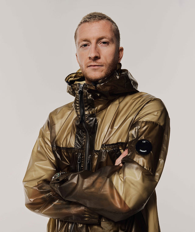 man wearing C.P. COMPANY PiUM Hooded Jacket featuring coated finish, semi-sheer panels, waterproof, signature Lens detail 