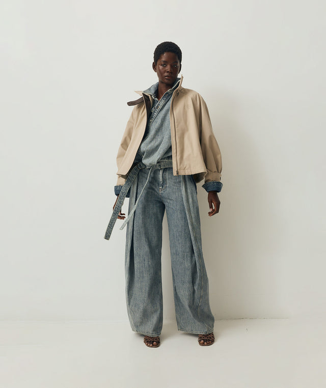 Person wearing a beige jacket, denim shirt, and wide-leg jeans by Loewe 