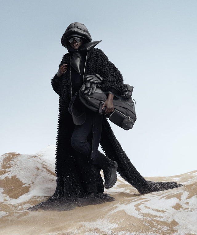 Moncler EE72 x Edward Enninful
campaign featuring a woman in sand wearing black cardigan, hood and storm boots 