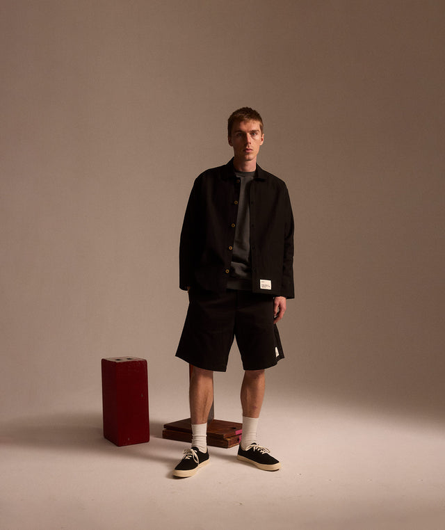 Man wearing black canvas chore coat, black shorts and black canvas sneakers all by OCD 27 