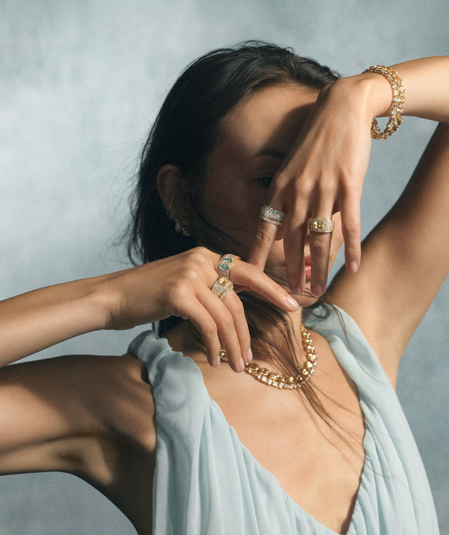 A model wearing multiple gold and diamond jewelry pieces by Renna, including a chain necklace, bracelet, and several statement rings 