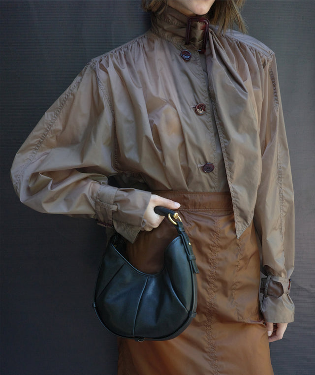 Woman wearing brown bow neck blouse, brown pencil skirt holding black leather handbag by Saint Laurent 
