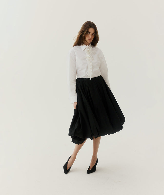 Woman wearing a white blouse and black skirt with Duchess pumps, all by Balenciaga 