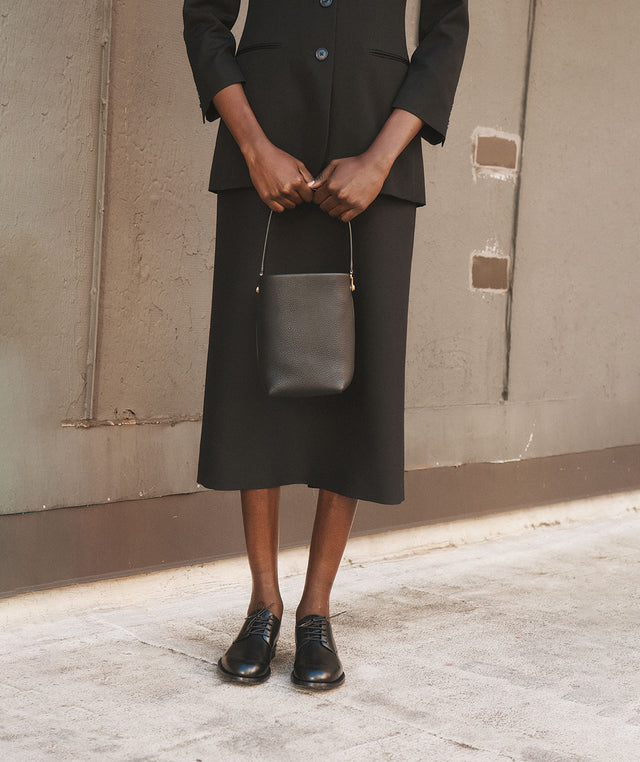 Woman wearing black skirt suit by The Row holding black tote bag 