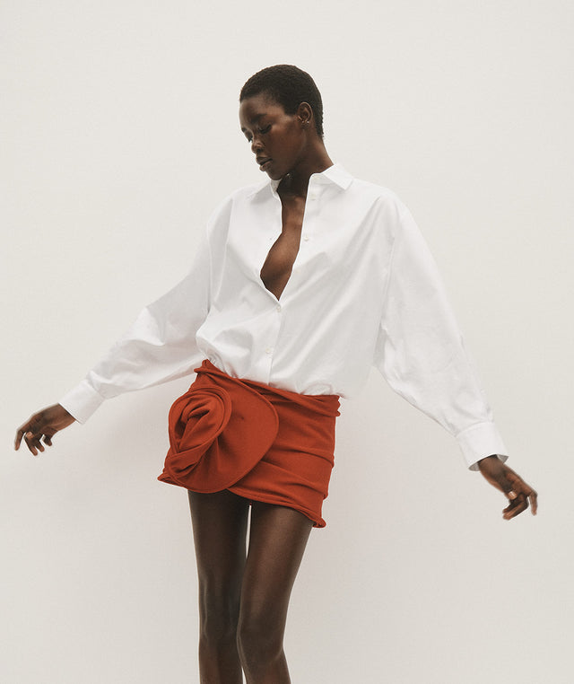 Woman wearing oversized white button-up shirt with red wool rose mini skirt, both by Magda Butrym 