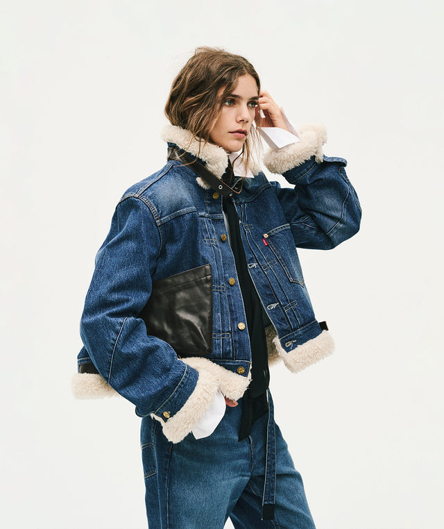 A model wearing Levi's X Sacai cropped blue denim jacket with cream shearling lining on the collar, cuffs, and hem 