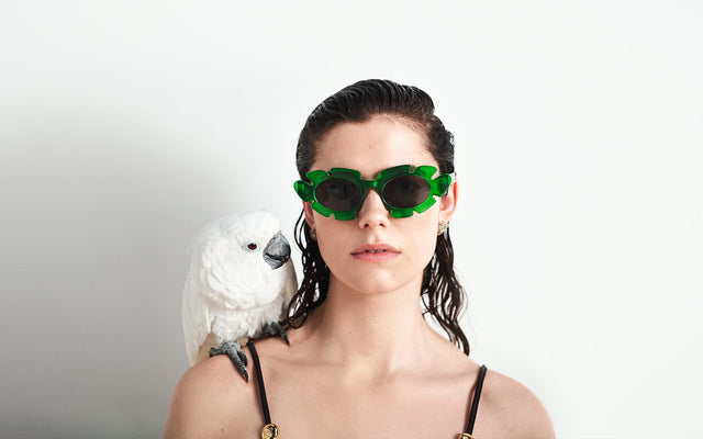 Woman wearing green leaf motif sunglasses with a parrot on her shoulder