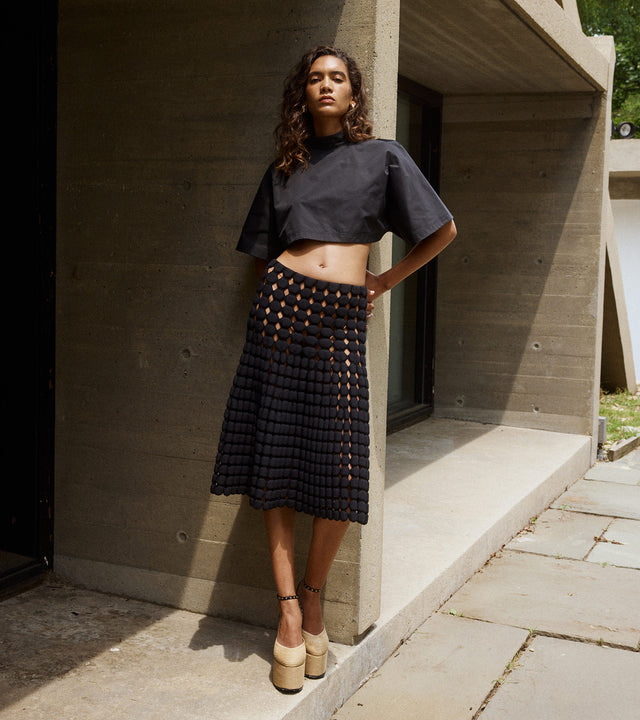 Woman wearing knit bubble skirt, cropped black top and platform espadrille sandals, all by Alaia 