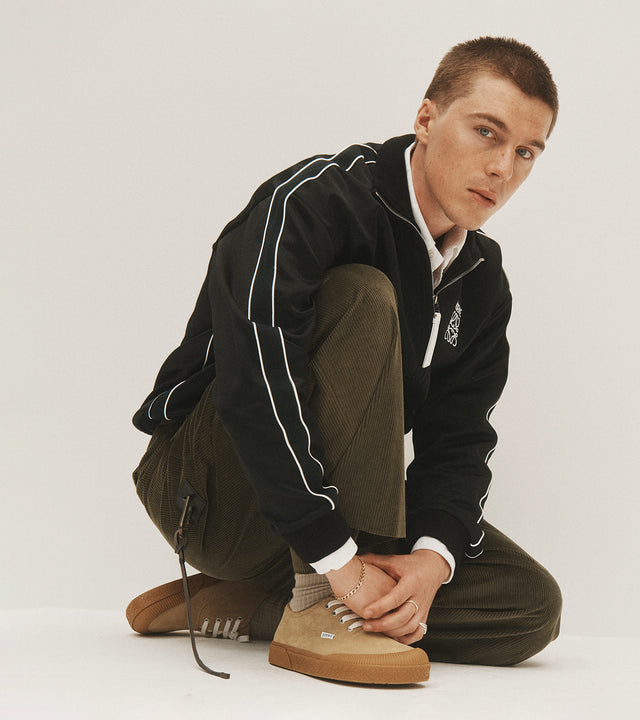 Man wearing Loewe track jacket, olive green pants, and suede Terra Vulca sneakers 