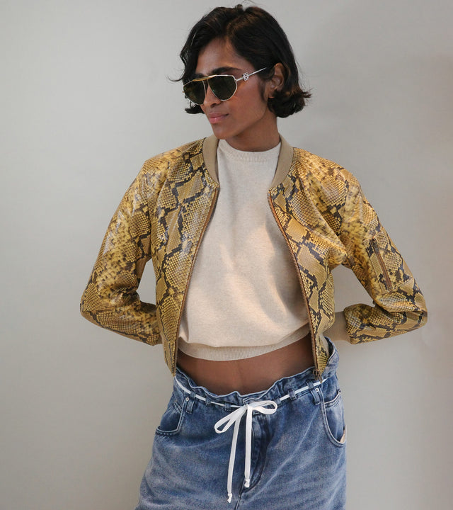 Woman wearing yellow and black snake print jacket and blue jeans with white tie belt, both by Isabel Marant 