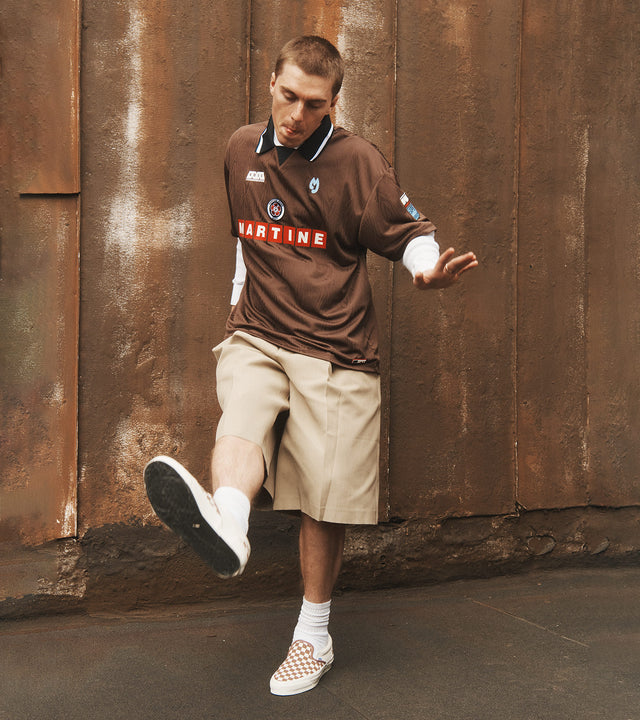 Man wearing Martine Rose football jersey, Jacquemus khaki shirts and checkered skip on Vans sneakers 