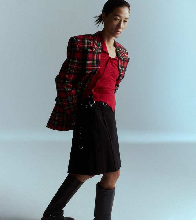 Woman wearing Saint Laurent red tartan blazer, Jacquemus red asymmetrical knit top, black Givenchy kilted skirt and Burberry knee-high boots