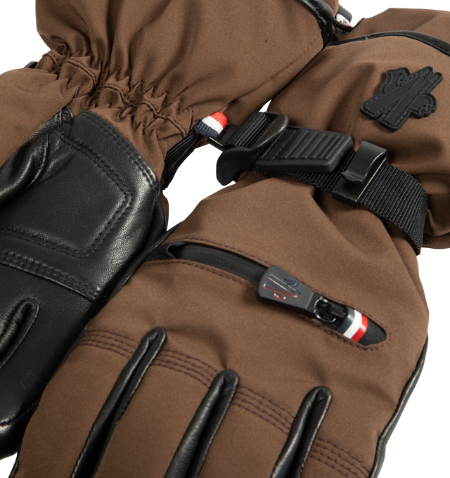 Image 3 of 3 - BROWN - Moncler Grenoble Women's Padded Gloves are crafted from a 4-way stretch technical nylon blend and feature a performance-driven design created in collaboration with Reusch. Engineered for mountain sports and ski conditions, these insulated gloves provide warmth and protection while leather reinforcements at the palms and fingertips enhance grip. Finished with a zipped pocket designed to hold a heating pad, adjustable cuffs, and a signature silicone logo patch. Main Material: 87% Polyam 