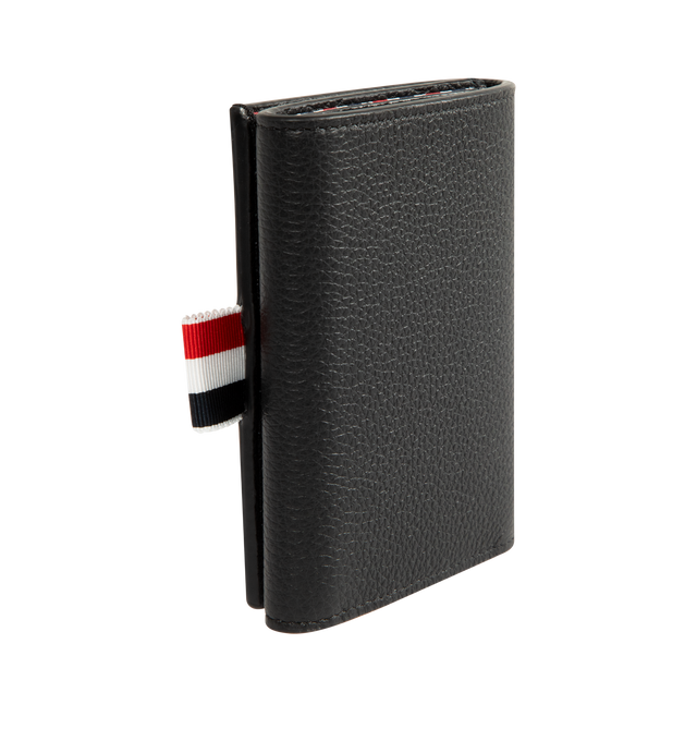 Image 2 of 3 - BLACK - THOM BROWNE Soft Pebble Grain Trifold Wallet featuring tricolor grosgrain flag at face, press-stud closure, four card slots, three patch pockets, one note slot, embossed logo at interior and Moir and tricolor grosgrain lining. H3.5" x W4.25". Leather. Made in Italy. 