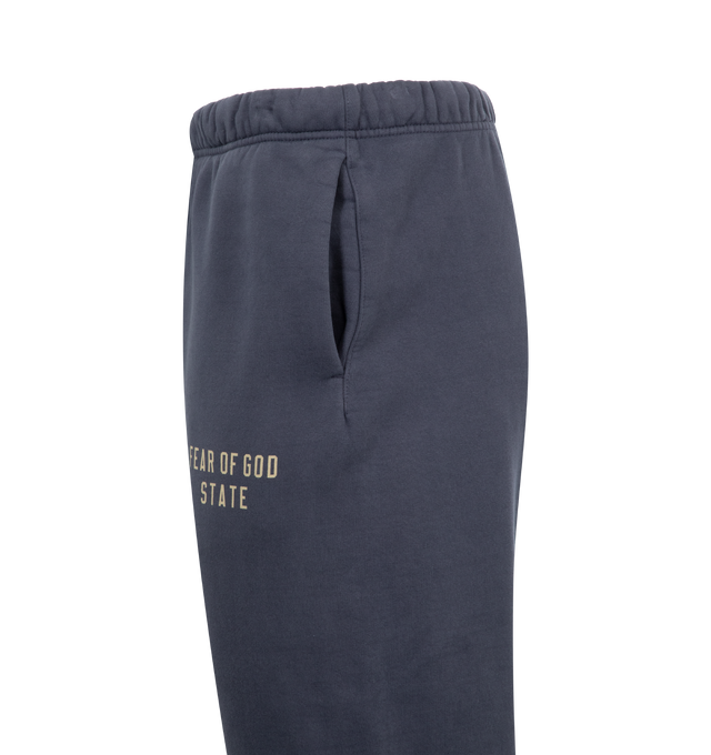 Image 3 of 3 - NAVY - Fear of God Essentials Heavy Fleece Sweatpants have an elastic drawstring waist, 3 stripe side panels, side pockets, elastic at the ankles, and a brand label. 83% cotton, 17% recycled polyester. 