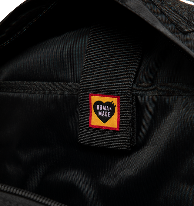 Image 3 of 3 - BLACK - Human Made Military Backpack is crafted from lightweight nylon Oxford fabric and features a military-inspired silhouette with stencil-style graphics and modular attachment functionality. Designed with a front flap pocket with buckle strap closure, a cushioned sleeve for a laptop or tablet, mesh-padded back panel, adjustable waist belt, and B4-sized storage capacity for everyday versatility. Main Material: Shell: 100% Nylon. Lining: 100% Polyester. Dimensions: 44 cm H x 32 cm W x 11 cm 