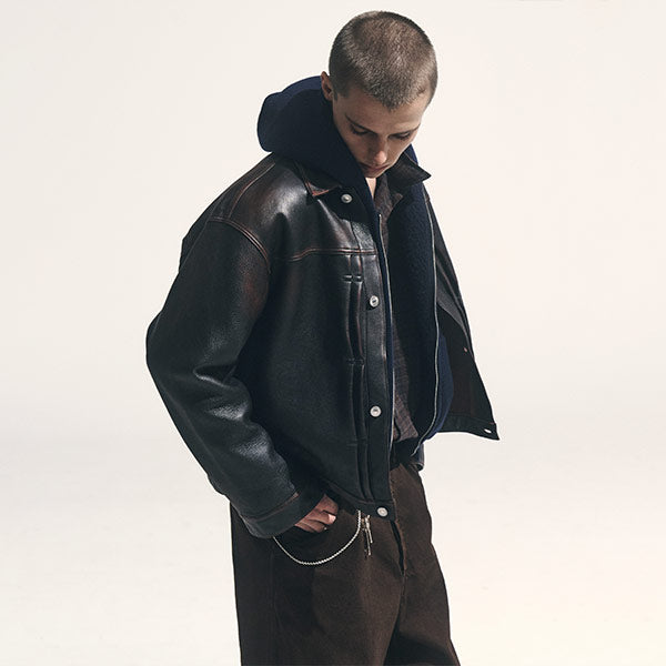 A model wearing a dark brown leather jacket, layered over a dark shirt and brown trousers, all by designer A.PRESSE