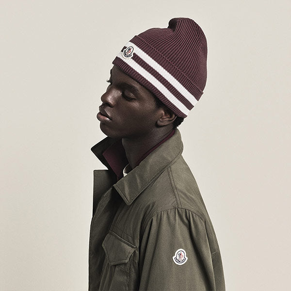 Person wearing a maroon beanie with a white stripe and a green jacket by Moncler