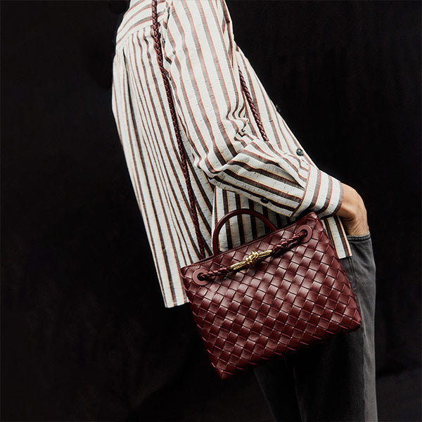 Person holding a woven brown Bottega Veneta handbag with a black background