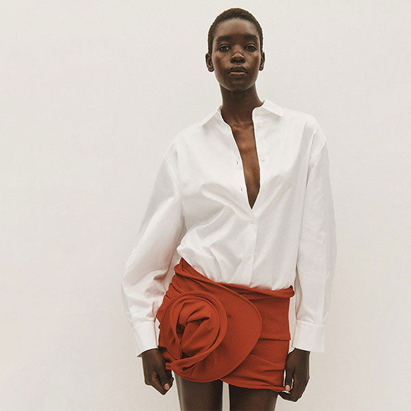 Woman wearing oversized white button-up shirt with red wool rose mini skirt, both by Magda Butrym