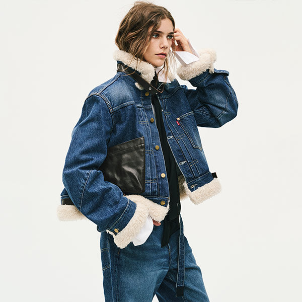 A model wearing Levi's X Sacai cropped blue denim jacket with cream shearling lining on the collar, cuffs, and hem