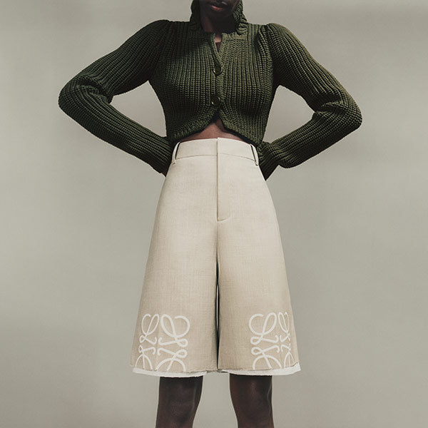 Woman wearing light beige shorts with anagram at each knee, by Loewe