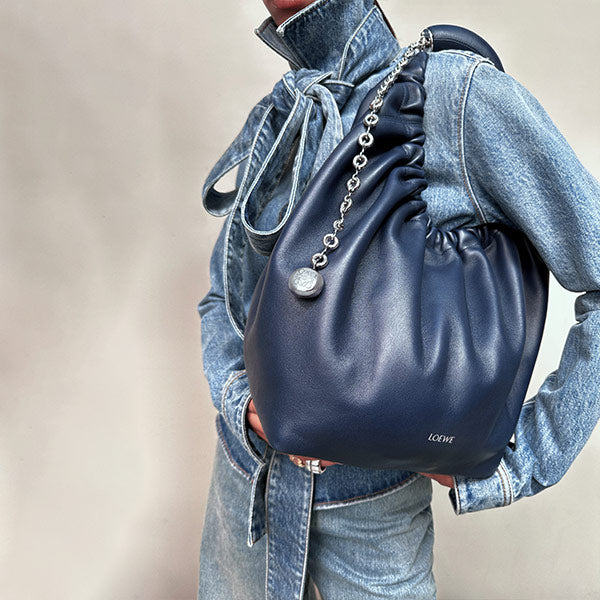 Woman wearing denim bow blouse carrying Navy blue leather squeeze bag, both by LOEWE