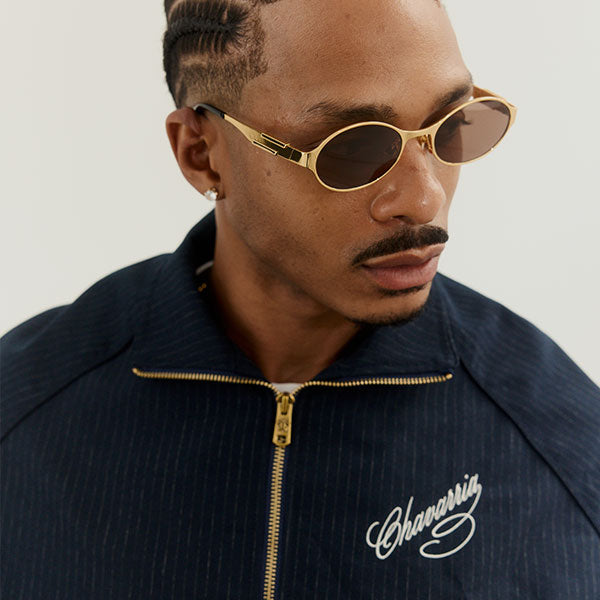 Man wearing gold sunglasses and a navy jacket with Chavarria branding.