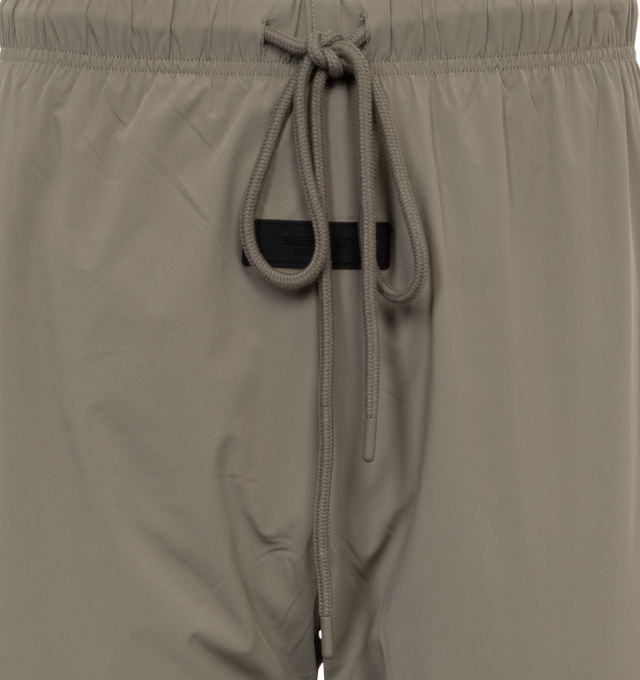 Image 4 of 4 - BROWN - Fear of God Essentials track pant made in stretch woven nylon and designed in a classic straight leg fit. Featuring rubberized label is at the center front, encased elastic waistband with elongated drawstrings with rubberized tips, side seam pockets, and ankle zippers. 86% Nylon, 14% spandex. 