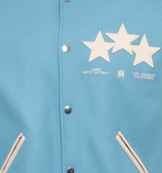 BLUE - AMIRI OVERSIZED STARS VARSITY JACKET crafted from durable light blue wool with leather contrast sleeves, adorned with a contellation of leather star appliques. Features contrast banded rib detailing at the waist, writsts and neck, welt zipper pockets, and classic snap button closure.  Wool shell, leather sleeves, viscose lining. Made in Italy. 