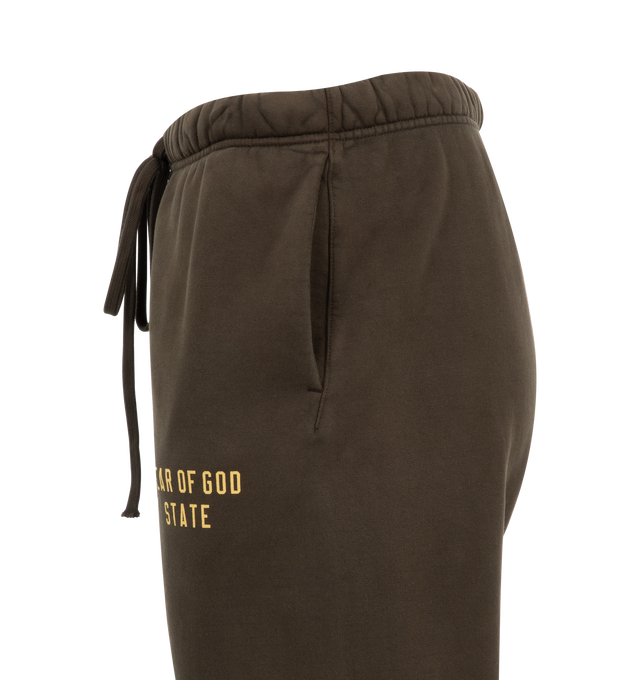 Image 3 of 3 - BROWN - Fear of God Essentials Heavy Fleece Sweatpants have an elastic drawstring waist, 3 stripe side panels, side pockets, elastic at the ankles, and a brand label. 83% cotton, 17% recycled polyester. 