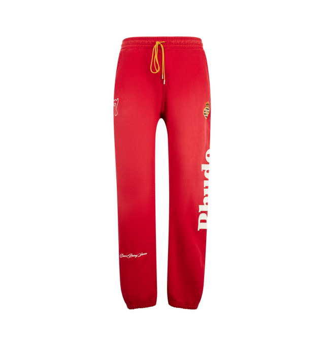 Image 1 of 4 - RED - Rhude Desert Racing Script Cuffed Sweatpant is crafted from cotton and features a relaxed silhouette with elasticated cuffs for a tapered fit. Designed with Desert Racing Script graphics, an elasticated waistband, and functional pocket detailing for everyday comfort. Main Material: 100% Cotton. Made in USA. 