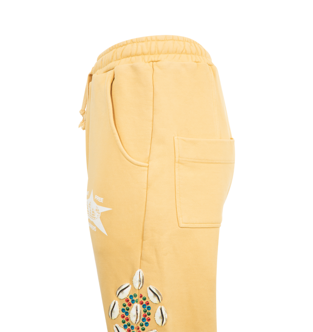 Image 3 of 3 - YELLOW - BARRIERS Cowrie Shell Sweatpants featuring heavyweight french terry, distressed garment dye, straight leg, diagonal side seam stitch, drawstring waistband, logo print at front, star in crackle distressed print and cowrie shells in puff print. 100% cotton. Made in USA. 
