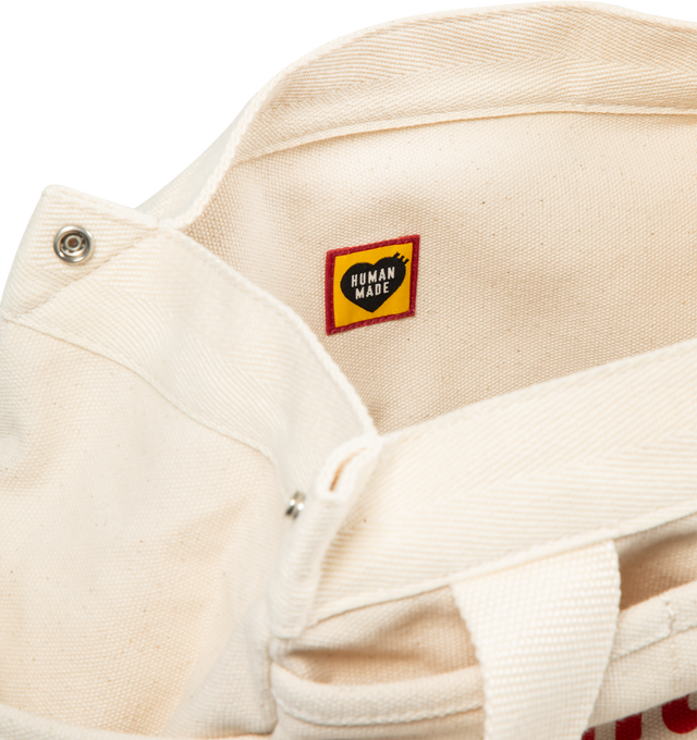 Image 3 of 3 - WHITE - HUMAN MADE Tool Bag featuring multi-pockets, made from thick, tough 18oz cotton canvas, convenient diagonal pockets below the heart patch, snap buttons for adjusting the gussets, handle also allows for shoulder carrying, graphics on both sides, Heart patch, heart name tag on the inside and A4-sized storage. 100% cotton. 