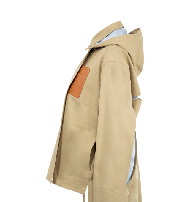 Image 3 of 3 - NEUTRAL - LOEWE Hooded Parka featuring water-repellent medium-weight cotton gabardine, relaxed fit, regular length, cut-out slits at the elbows and at the back revealing striped cotton poplin lining, detachable hooded collar with drawstring, belted cuffs, button front fastening with foldover panel, patch pockets, back pleat, asymmetric front to back hem, side slits with ties and LOEWE Anagram embossed leather patch pocket placed on the chest. 100% cotton. Made in Italy. 