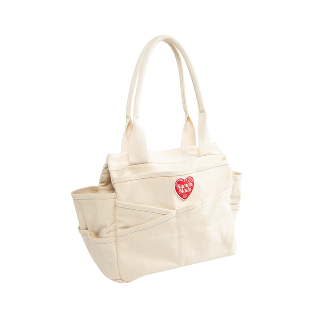 Image 2 of 3 - NEUTRAL - Human Made Tool Bag is crafted from durable 20oz cotton canvas and features a tote-style silhouette with multiple diagonally cut utility pockets for everyday organization. Designed with pigment-printed graphics, a signature heart patch, side snap buttons for adjusting the gusset, and spacious A4-sized storage capacity. Main Material: 100% Cotton. Dimensions: 25 cm H  31 cm W  19 cm D. Fits: notebooks, tablet, water bottle, wallet, phone, and daily essentials.  