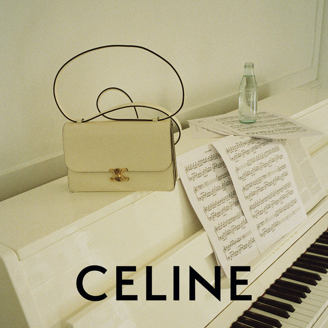 A Celine shoulder bag in light beige with a gold interlocking CC clasp and a thin black strap, styled on a white piano next to sheet music and a glass bottle, with the word CELINE in bold text at the bottom. 