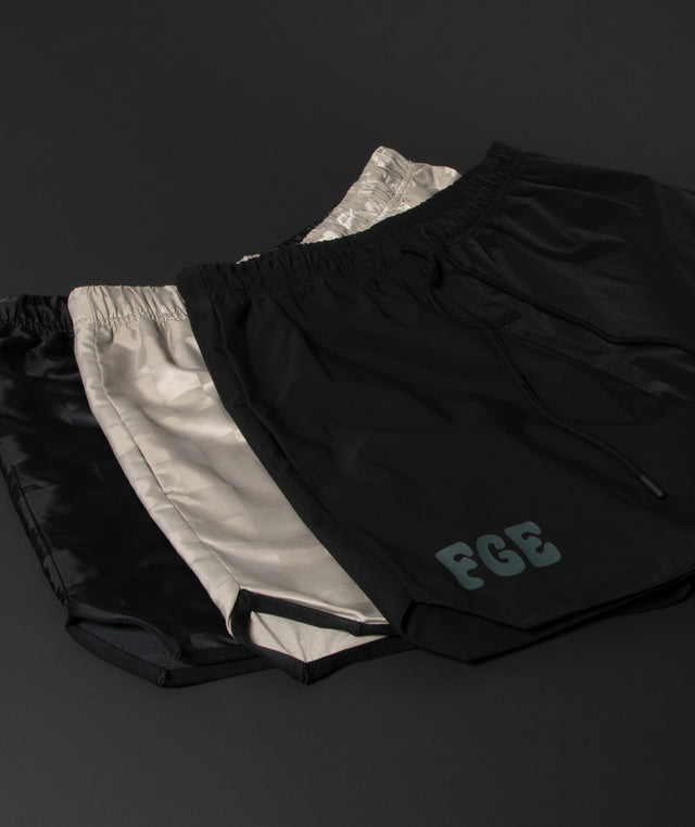 Three pairs of athletic shorts in black and metallic silver by Fear of God with 'FGE' logo on the left leg. 
