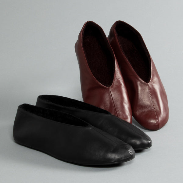 Two slip-on slipper-style shoes by The Rowone pair in black leather with dark lining in front, and one pair in dark burgundy leather with dark lining behind.