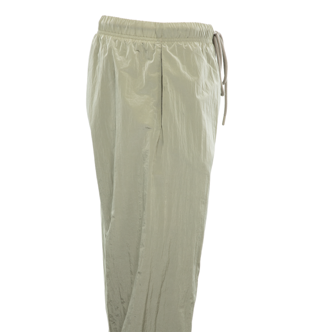 Image 3 of 4 - GREEN - FEAR OF GOD ESSENTIALS Crinkle Nylon Trackpants featuring an encased elastic waistband with elongated drawstrings, side seam pockets, an elastic hem with zipper adjustability at the ankle and a rubberized label at the center front. 100% nylon.  