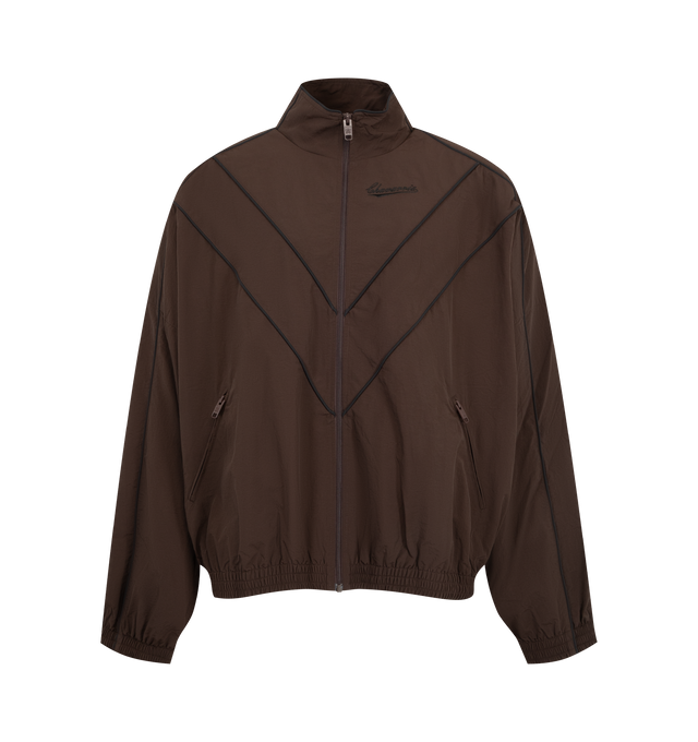Image 1 of 3 - BROWN - Willy Chavarria Bad Boy Track Jacket is crafted from nylon and features a sleek, true-to-size silhouette defined by bold chevron paneling and contrast piping. Designed with a stand collar, front zip closure, two zippered pockets, stacked script logo detailing, and elasticized cuffs and hem. Main Material: 100% Nylon. Lining: Polyester. 
