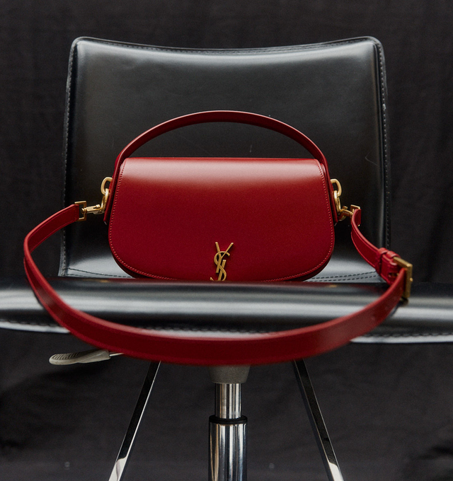 Image 2 of 5 - RED - SAINT LAURENT Mini Voltaire half-moon shoulder bag in calfskin with gently polished finish. Features a flap with magnetic Cassandre hinge closure and one flat interior pocket. Calfskin leather with leather lining and bronze-tone hardware. Made in Italy. Measures 8.3" X 4.3" X 1.8" with 9.4" strap drop.  