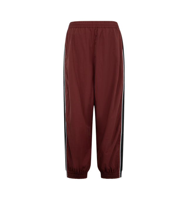 Image 2 of 3 - RED - Willy Chavarria Bad Boy Track Pant is crafted from lightweight nylon and features a relaxed athletic silhouette with an elasticated waistband and cuffs. Designed with a concealed drawstring waist, two seam pockets, embroidered logo detailing, and contrast piping along the outseams, the pant delivers the brand's bold sportswear-inspired aesthetic. Main Material: 100% Nylon.  