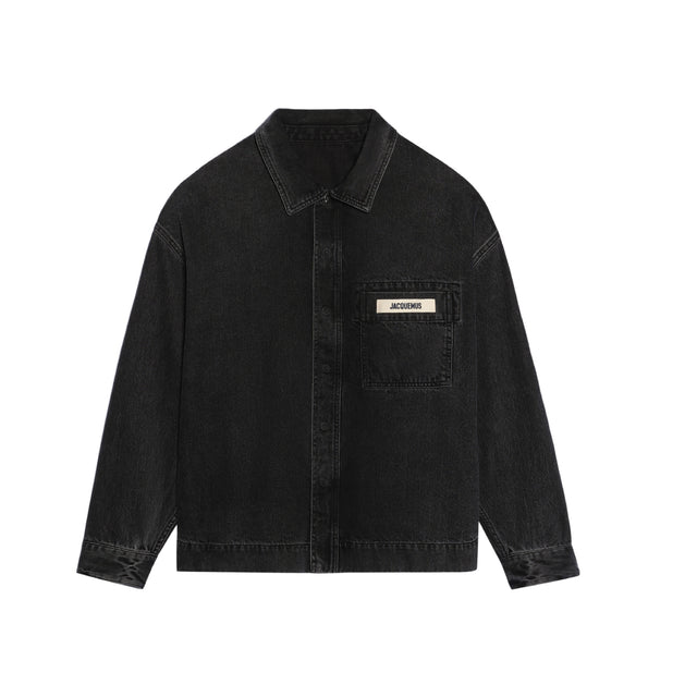 Image 1 of 1 - BLACK - JACQUEMUS La Chemise de-Nmes Jacket featuring boxy fit, over-dyed black denim, pointed collar, hidden snap button placket with one visible button, snap buttoned cuffs, chest patch pocket with embroidered grosgrain logo and silver metal hardware. 100% cotton. Made in Portugal. 